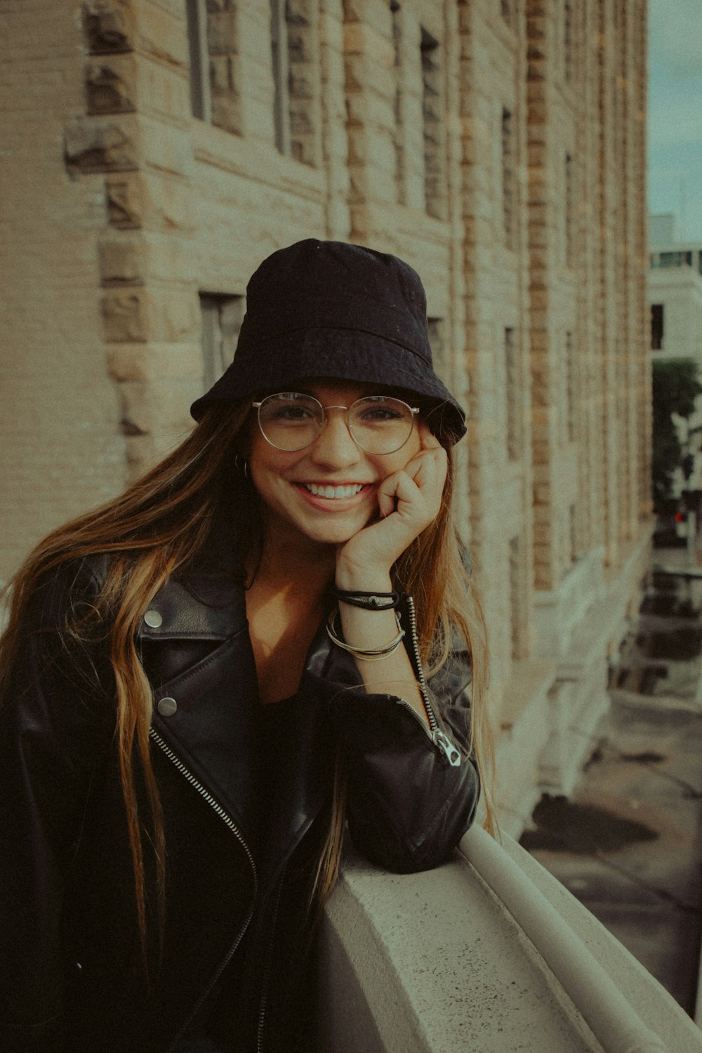 woman in black leather jacket wearing black framed eyeglasses and black hat