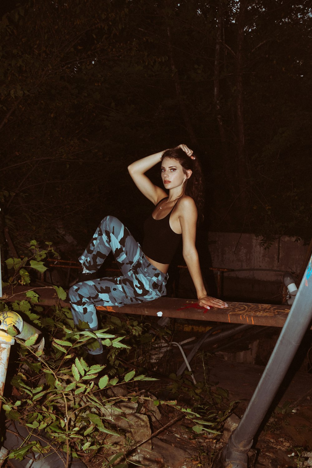 woman in black tank top and blue pants sitting on brown wooden bridge