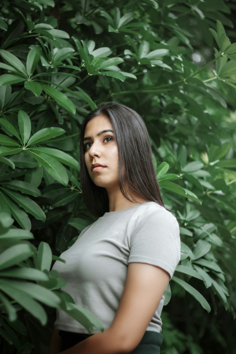 woman in white crew neck t-shirt standing near green leaves