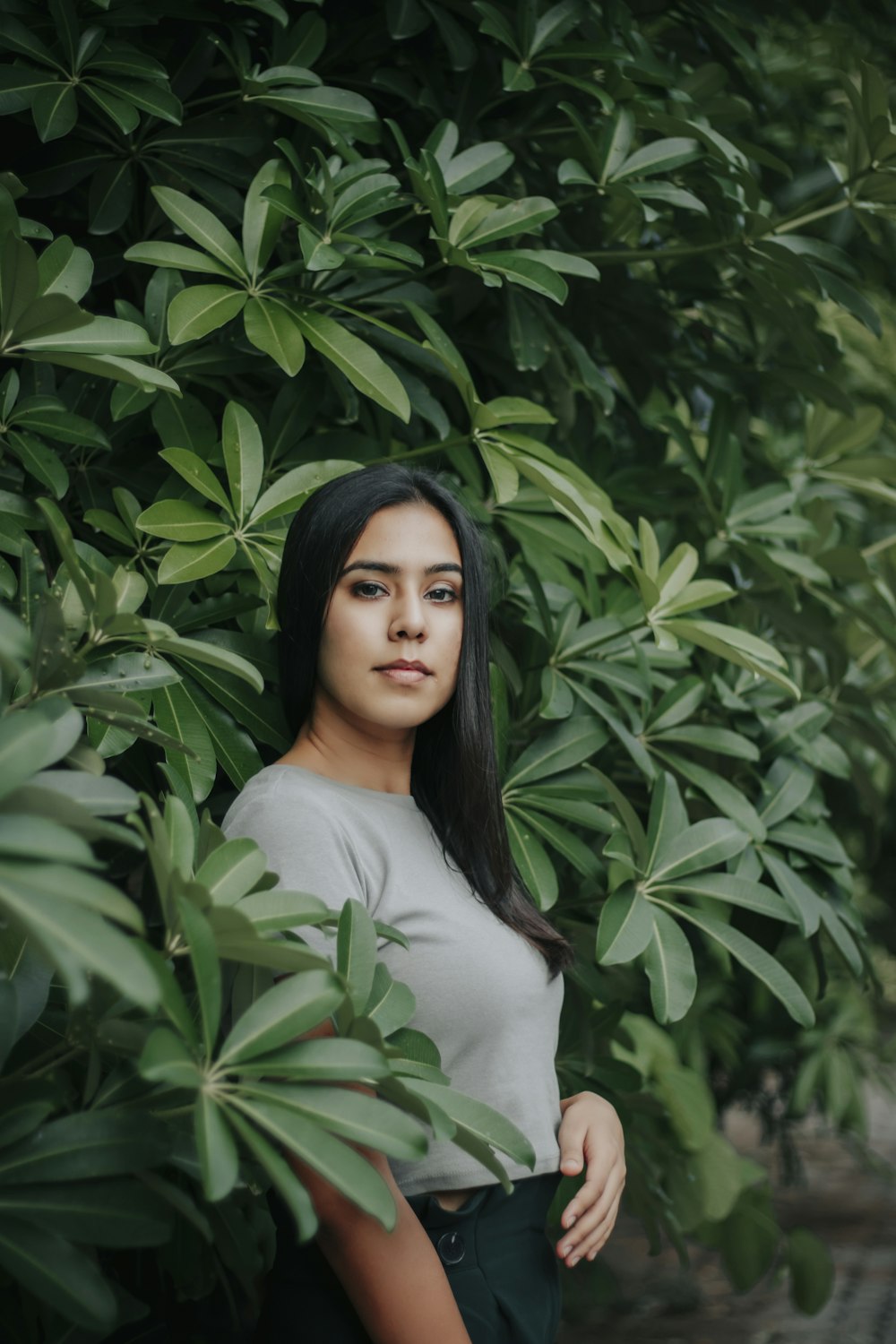 woman in white crew neck shirt standing beside green leaves
