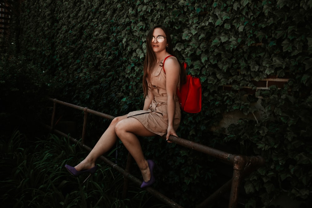 woman in brown dress sitting on black metal fence