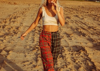 woman in white tank top and red and black plaid pants standing on brown sand during