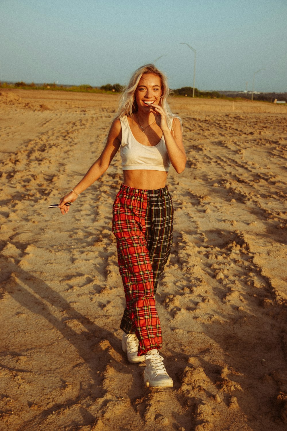 woman in white tank top and red and black plaid pants standing on brown sand during