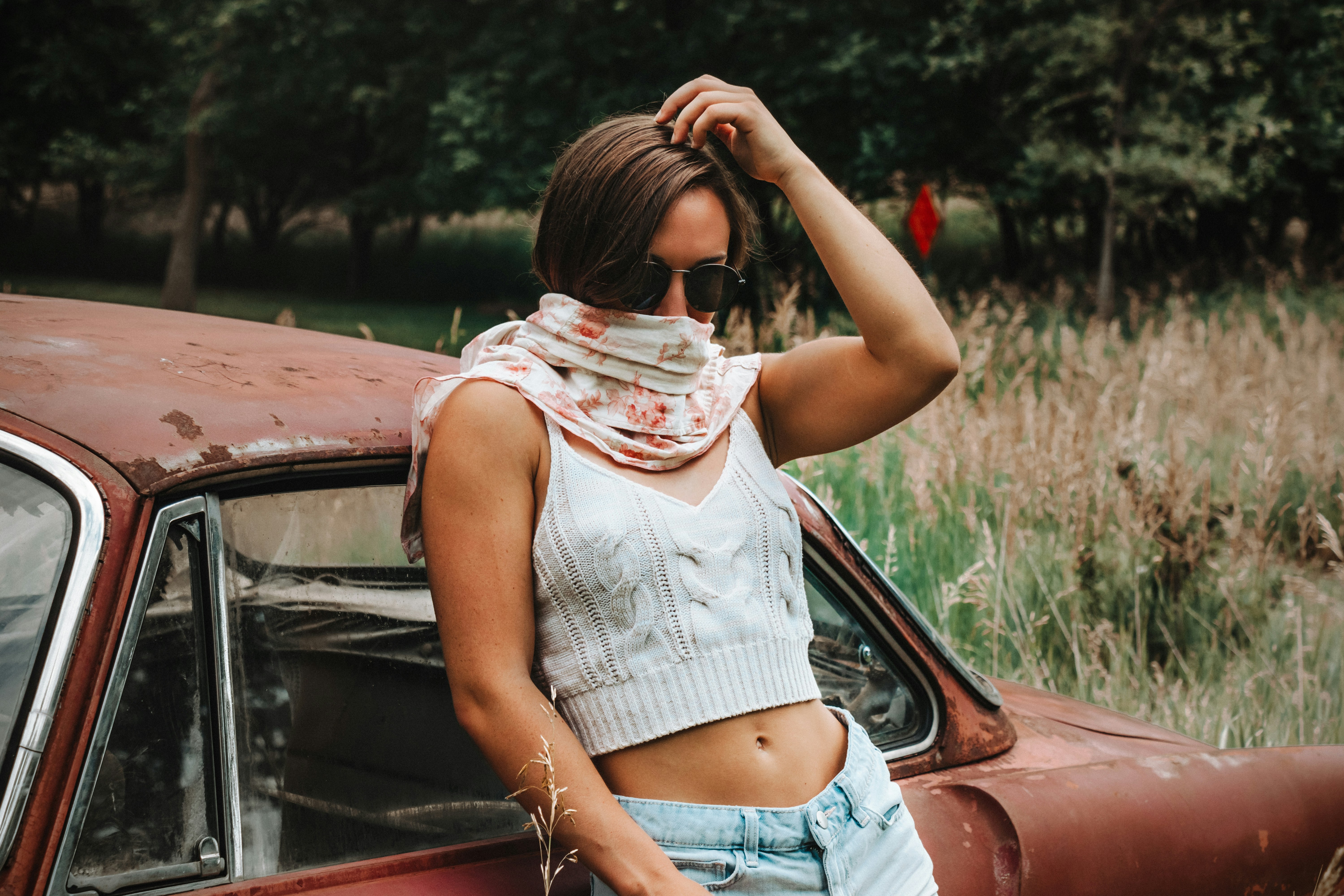 woman in white tank top and blue denim shorts sitting on red car