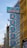 A series of vertical blue signs with red text displayed on the side of a building, featuring Chinese characters. The building has a modern architectural design with glass windows and a distinctive yellow facade. There are ornamental features and some greenery visible in the vicinity.
