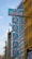A series of vertical blue signs with red text displayed on the side of a building, featuring Chinese characters. The building has a modern architectural design with glass windows and a distinctive yellow facade. There are ornamental features and some greenery visible in the vicinity.