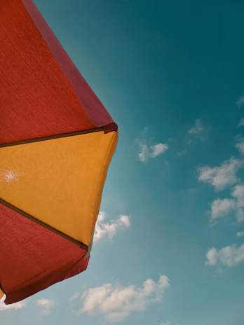 A vibrant red foldable umbrella open against a sunny blue sky.