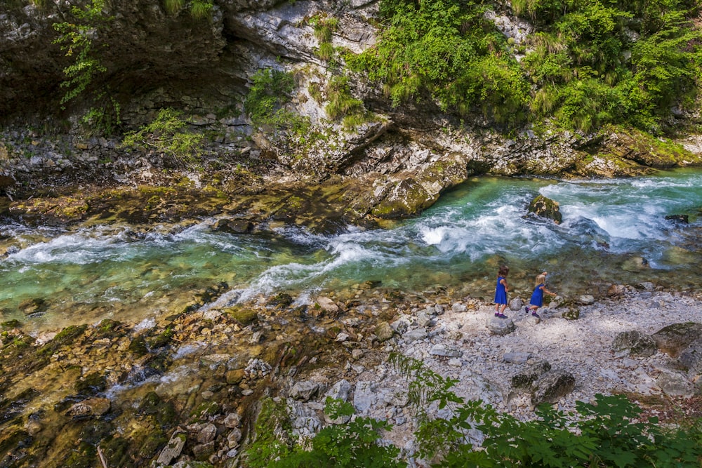 2 person standing on rocky river during daytime