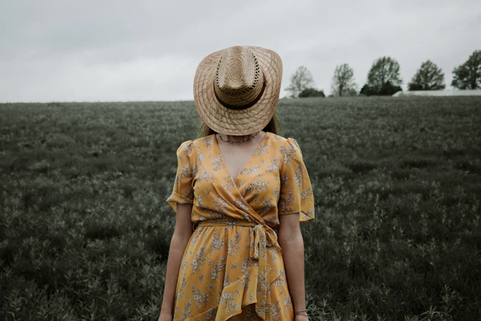 Woman in a yellow and red floral dress and straw hat on a grass field
