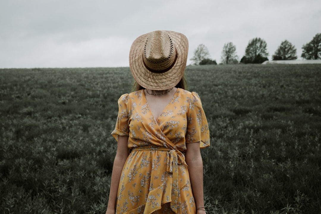 woman in yellow and red floral dress wearing brown straw hat standing on green grass field