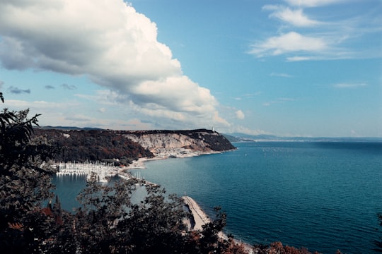 body of water near mountain under blue sky during daytime in Trieste Italy