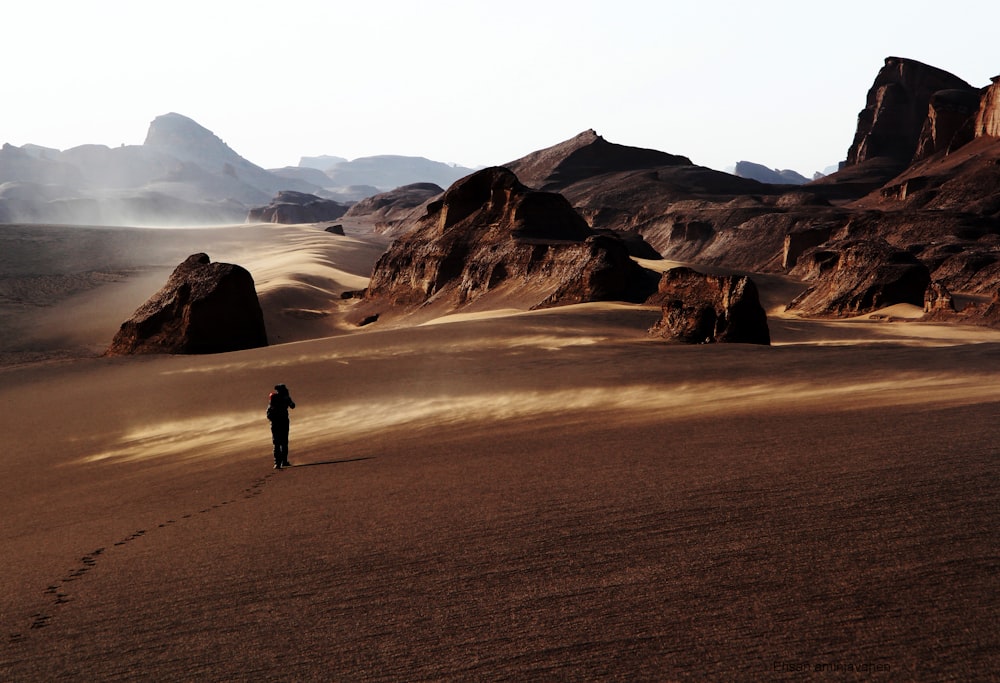 person walking on brown sand near brown mountain during daytime