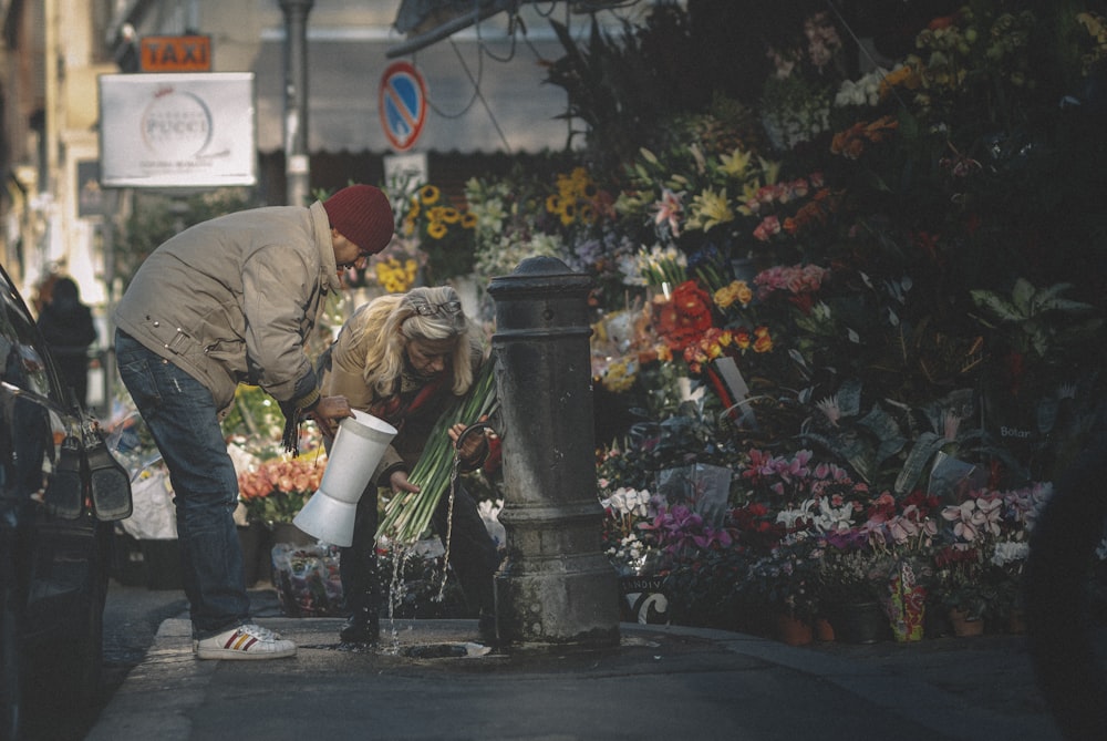 woman in gray jacket sitting on black concrete bench near red flowers during daytime