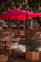 A vibrant red awning shading a cozy outdoor café seating area on a sunny day.