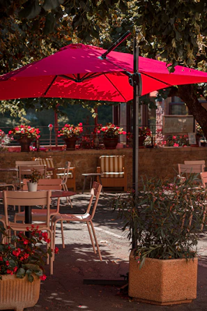 A vibrant red awning shading a cozy outdoor café seating area on a sunny day.