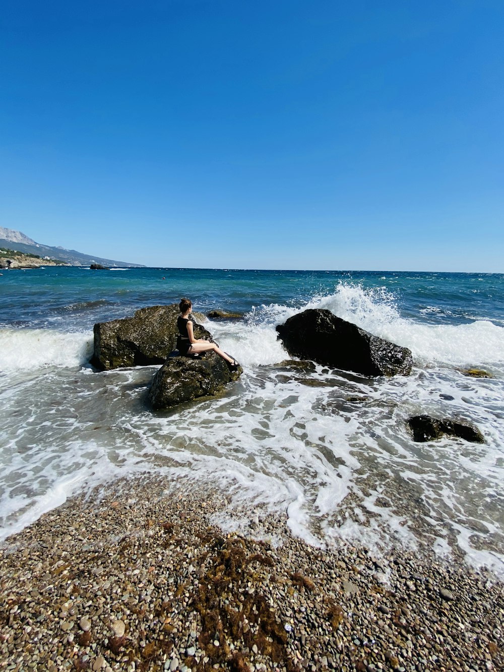 Frau in schwarzem Kleid, die tagsüber auf einer Felsformation auf See sitzt