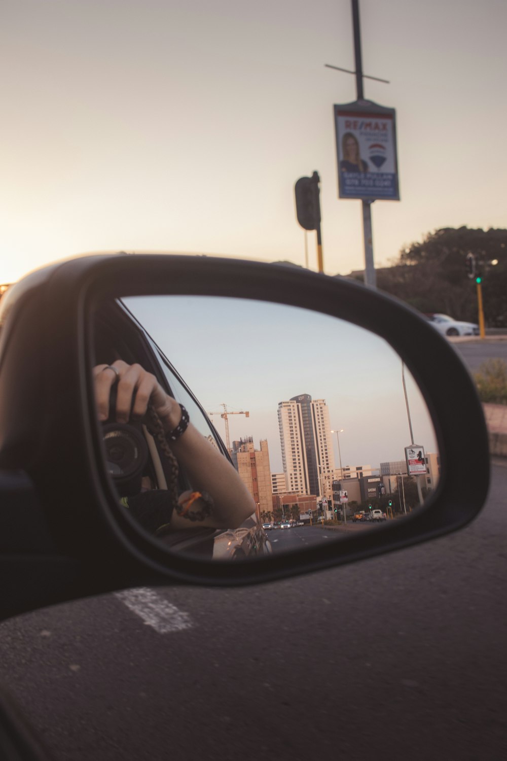car side mirror showing city buildings during sunset