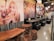A cozy dining area features rustic wooden tables and stools combined with modern, black cushioned seating. The walls are adorned with large, vibrant images of people enjoying pizza and artistic renderings of pizza slices. Ambient lighting with multiple hanging spherical lights adds warmth and an inviting atmosphere.