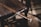 An intricately designed sword with a wooden handle is laid across a wooden chair. The sword's hilt is detailed with metal craftsmanship. The setting has a rustic and historical feel, with shadows cast by natural light.
