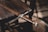 An intricately designed sword with a wooden handle is laid across a wooden chair. The sword's hilt is detailed with metal craftsmanship. The setting has a rustic and historical feel, with shadows cast by natural light.
