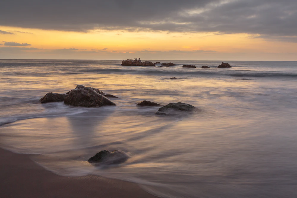 Olas suaves sobre rocas en la orilla durante un atardecer dorado