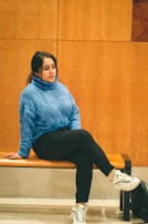 A casual outfit laid out on a wooden bench: soft knit sweater, slim pants, and sleek sneakers.