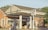A gas station with Gulf branding, featuring two fuel pumps beneath a canopy. The brick building in the background has large windows. There are signs with fuel prices and various advertisements. The scene is lit by warm, natural sunlight.