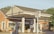 A gas station with Gulf branding, featuring two fuel pumps beneath a canopy. The brick building in the background has large windows. There are signs with fuel prices and various advertisements. The scene is lit by warm, natural sunlight.