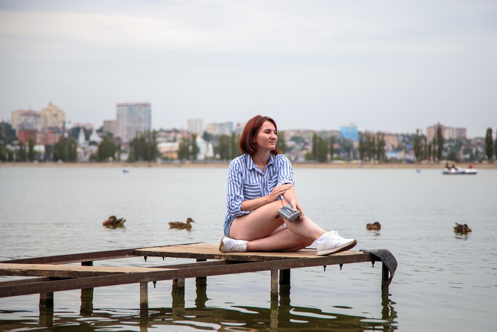 woman in blue and white stripe shirt sitting on brown wooden bench near body of water