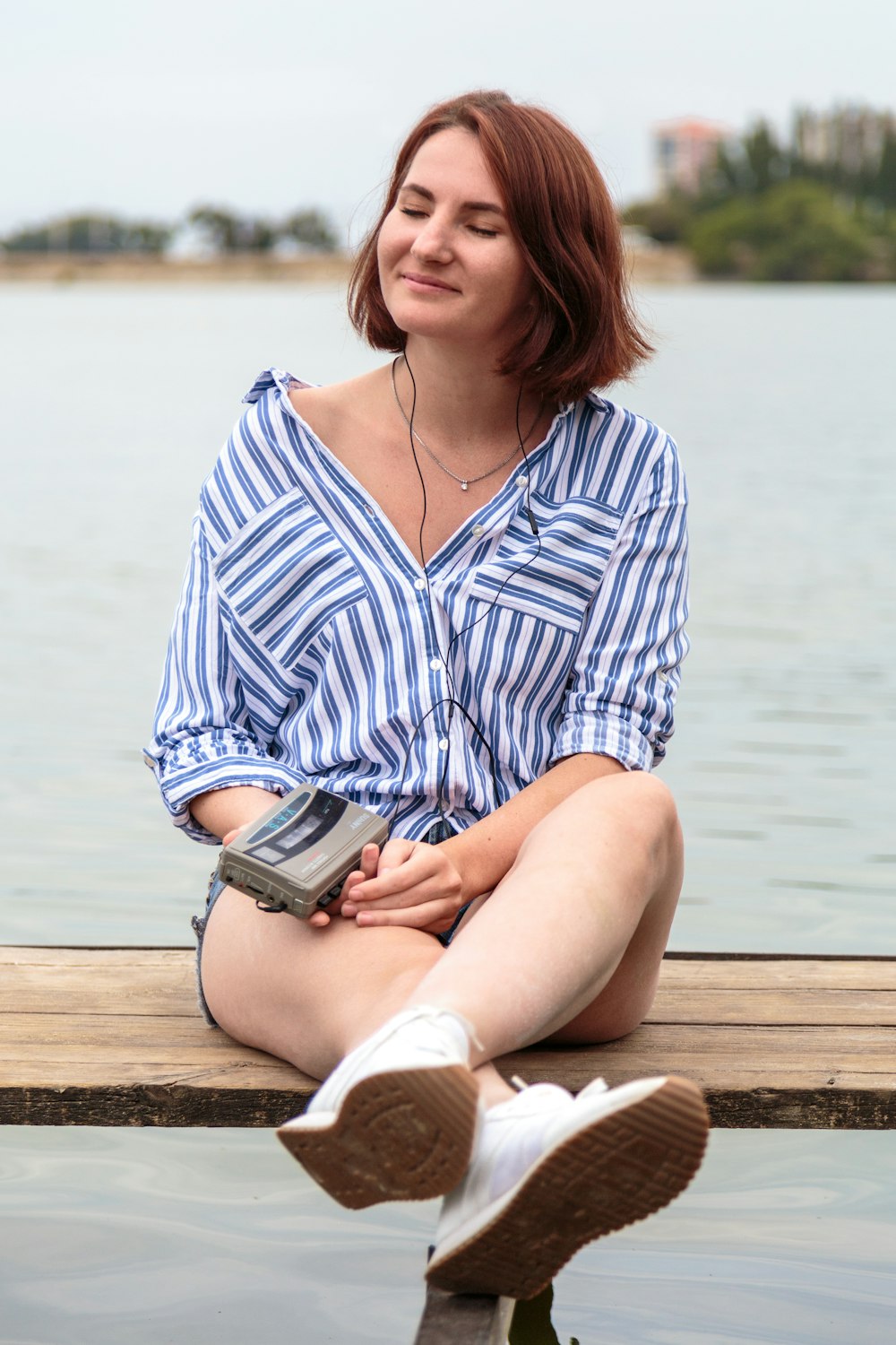 woman in blue and white striped long sleeve shirt sitting on brown wooden dock during daytime
