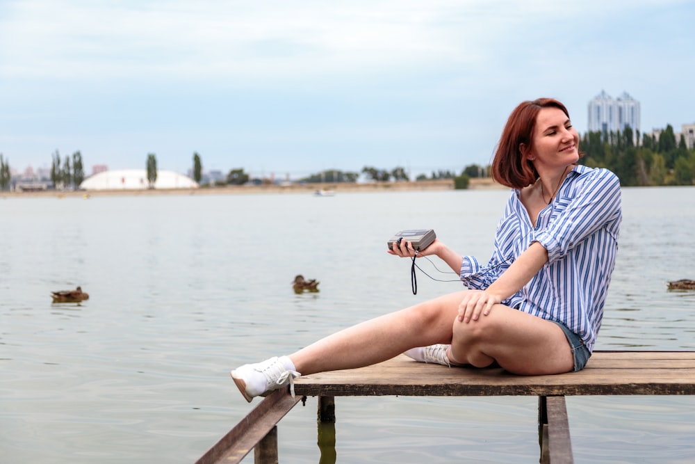 woman in blue and white dress sitting on brown wooden bench near body of water during
