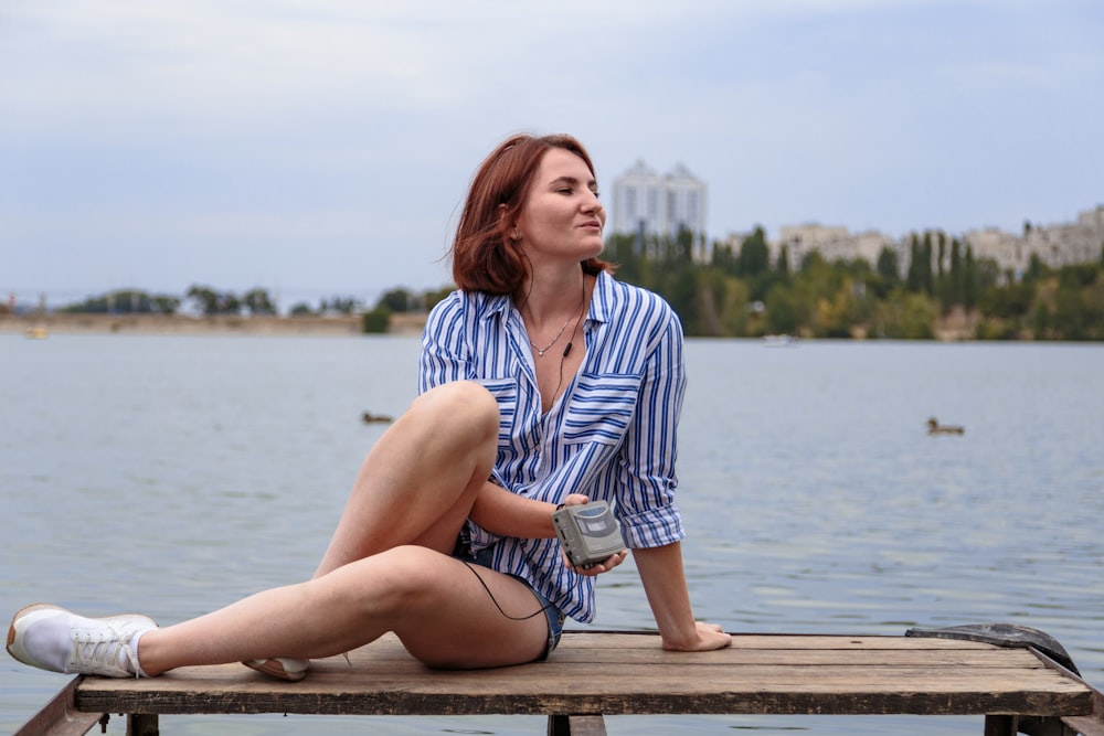 woman in blue and white stripe dress shirt sitting on brown wooden dock during daytime