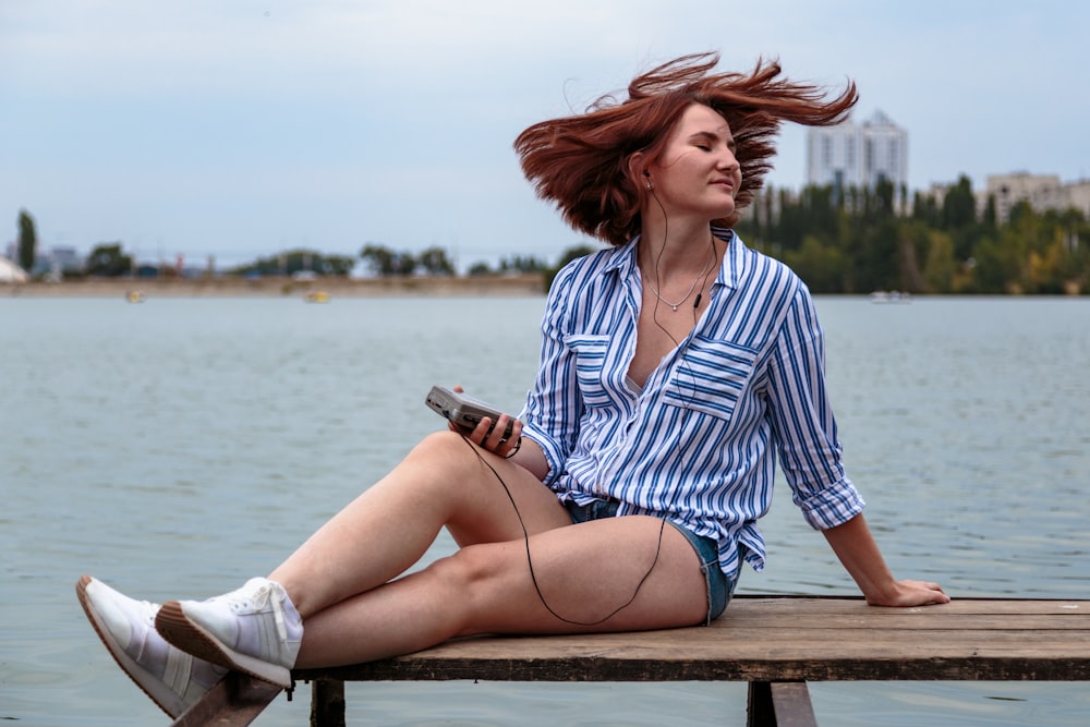 woman in white and blue striped dress shirt sitting on brown wooden bench