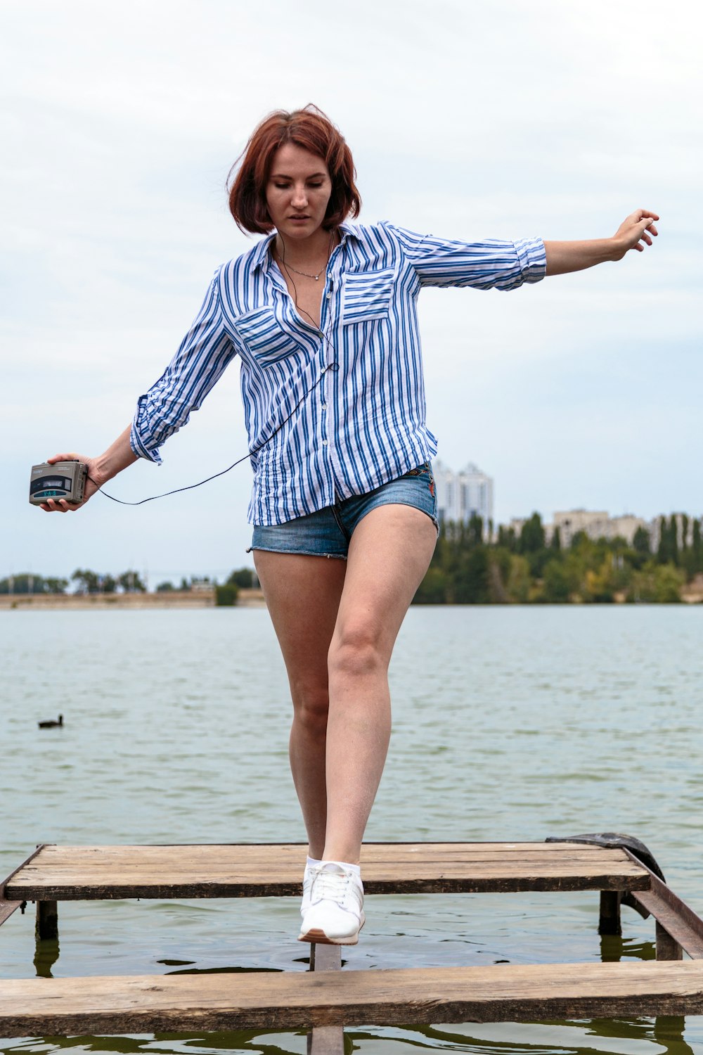 Donna in camicia a maniche lunghe a righe bianche e blu e pantaloncini in denim blu in piedi su marrone