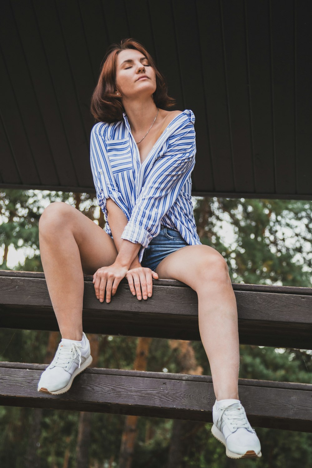 mulher na camisa social da listra azul e branca sentada no banco de madeira marrom