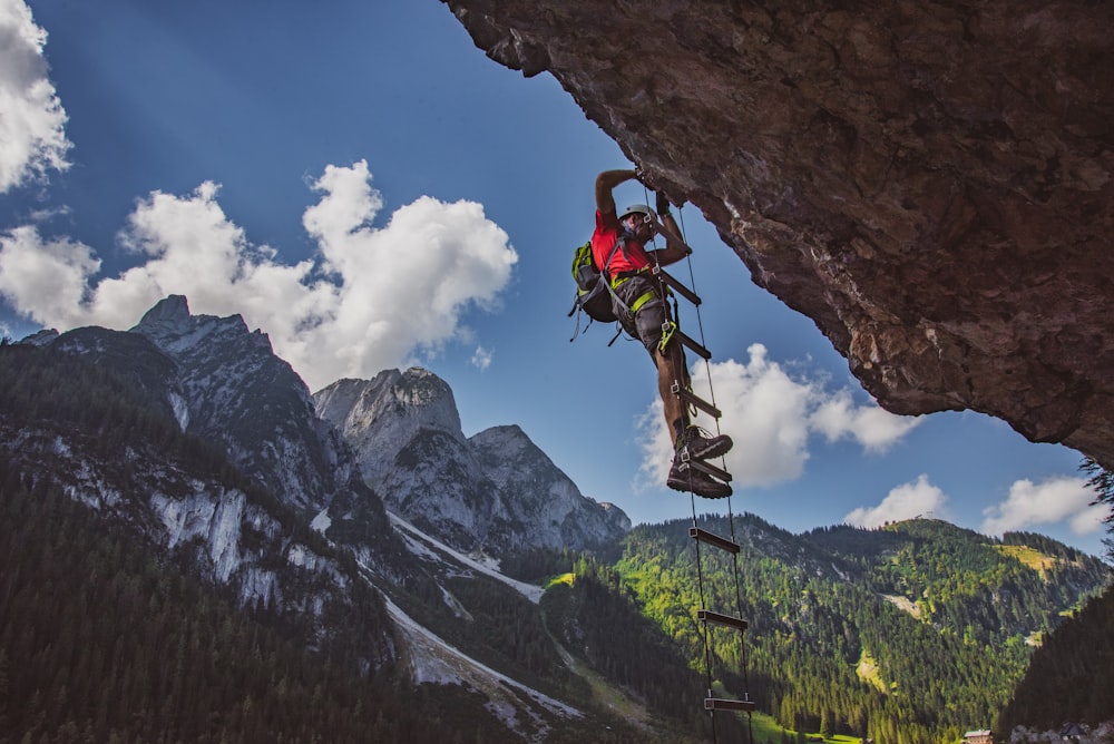 man in red shirt and blue shorts climbing mountain during daytime