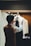 A person wearing a brown vest adjusts a dark tie on a mannequin dressed in a white shirt, situated in a well-lit tailor shop with wooden and cloth decor.