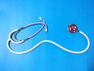A stethoscope with a pink chest piece and white tubing is laid out on a vibrant blue surface. The tubing forms a curved shape, and the earpieces are slightly visible.
