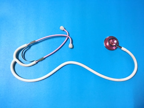A stethoscope with a pink chest piece and white tubing is laid out on a vibrant blue surface. The tubing forms a curved shape, and the earpieces are slightly visible.