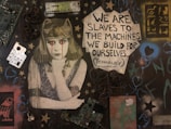 A mural features an image of a figure with an ancient Egyptian headdress, depicted with tears of technology components. The background is filled with various objects like circuit boards, metal scraps, and painted symbols. A prominent text reads, 'We are slaves to the machines we build for ourselves... (Technology),' surrounded by star and heart motifs.