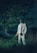 A person wearing a gas mask and protective suit stands in a grassy area at night. The figure holds a device emitting smoke, surrounded by tall grasses and a tree.