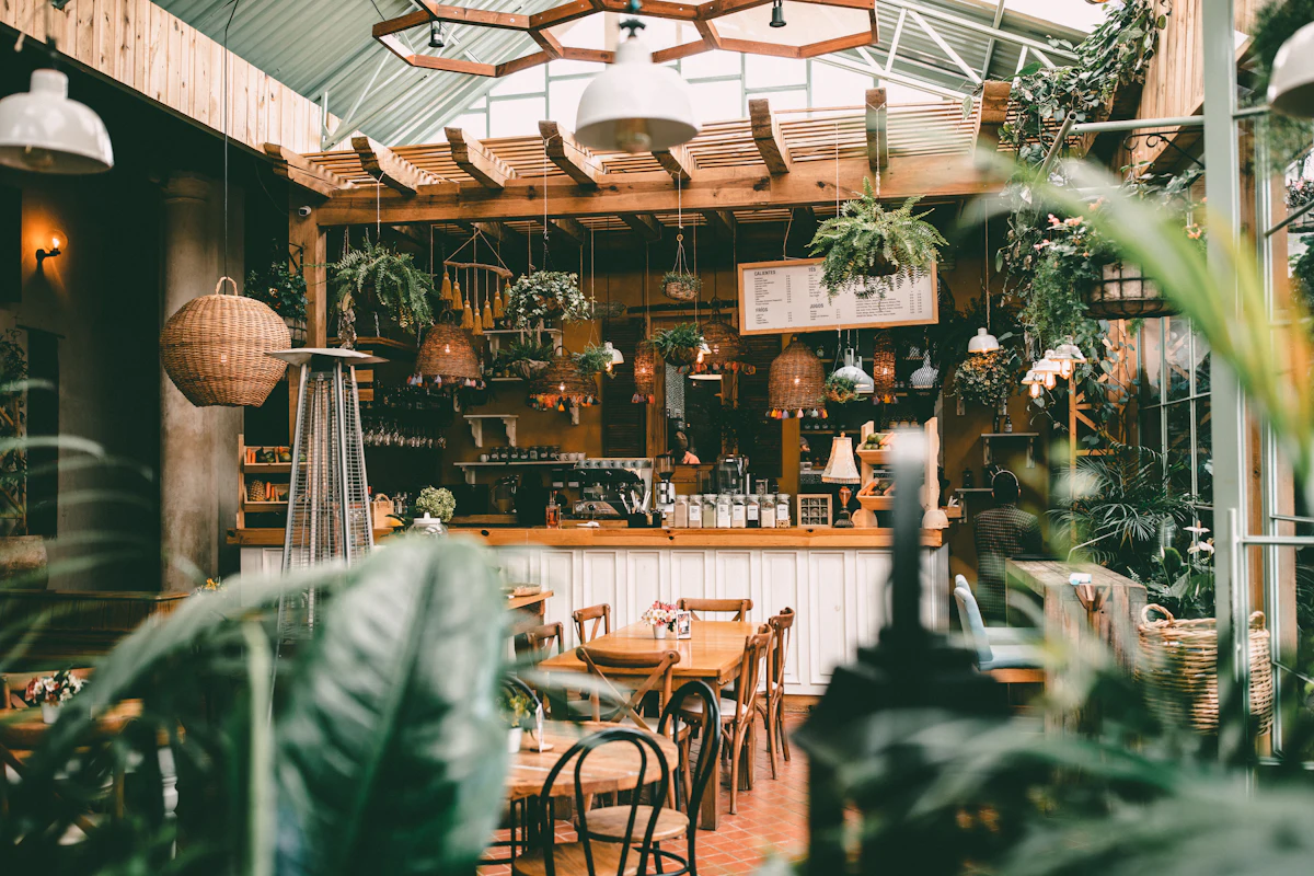 Interior del café: mesas de madera, plantas colgantes y barra al fondo