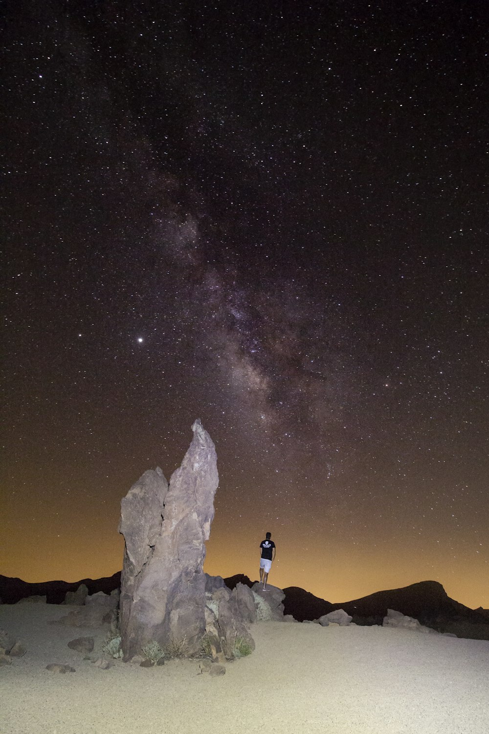 Silhouette von Menschen, die unter sternenklarer Nacht auf dem Berg stehen