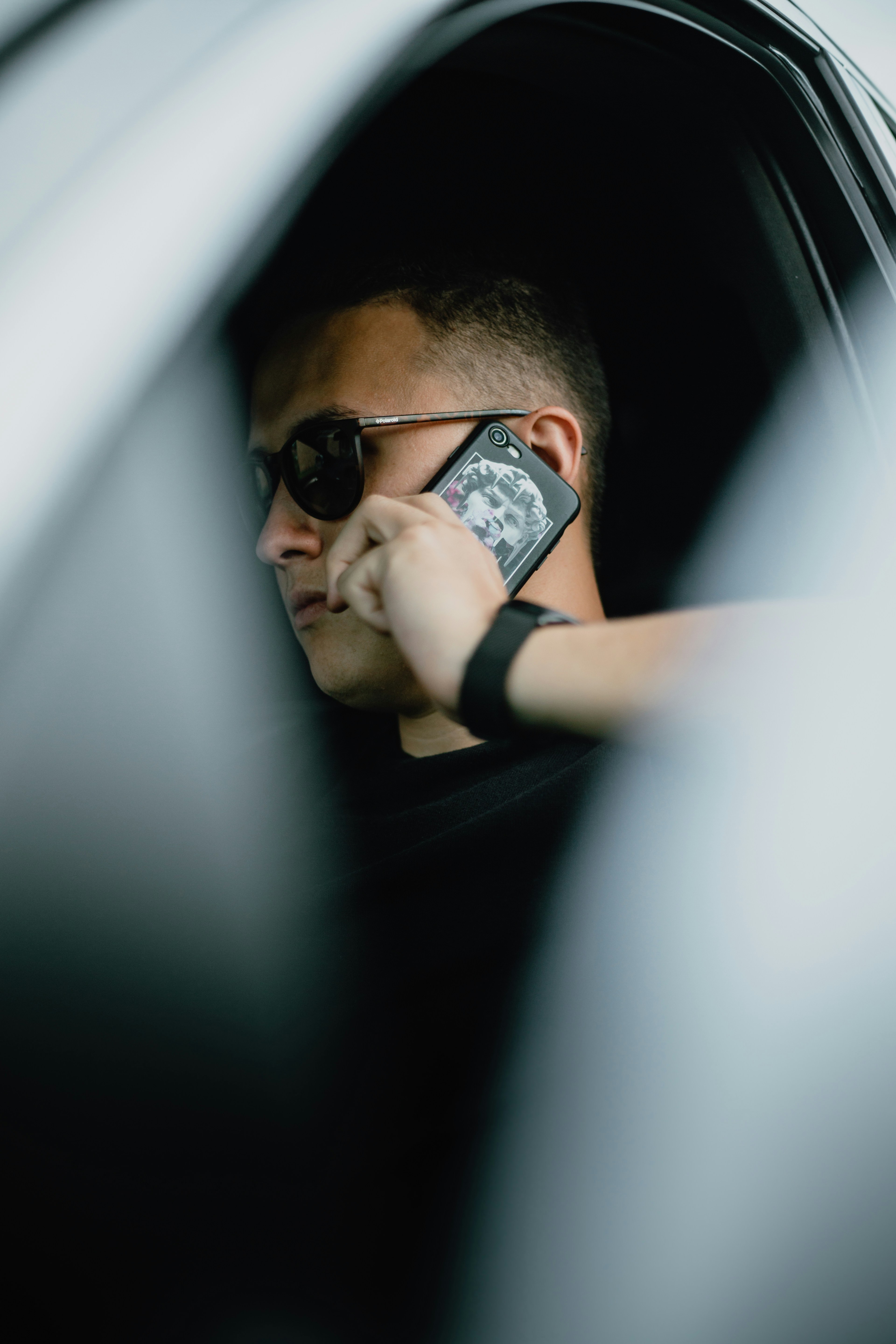 man in black shirt wearing black sunglasses holding black smartphone