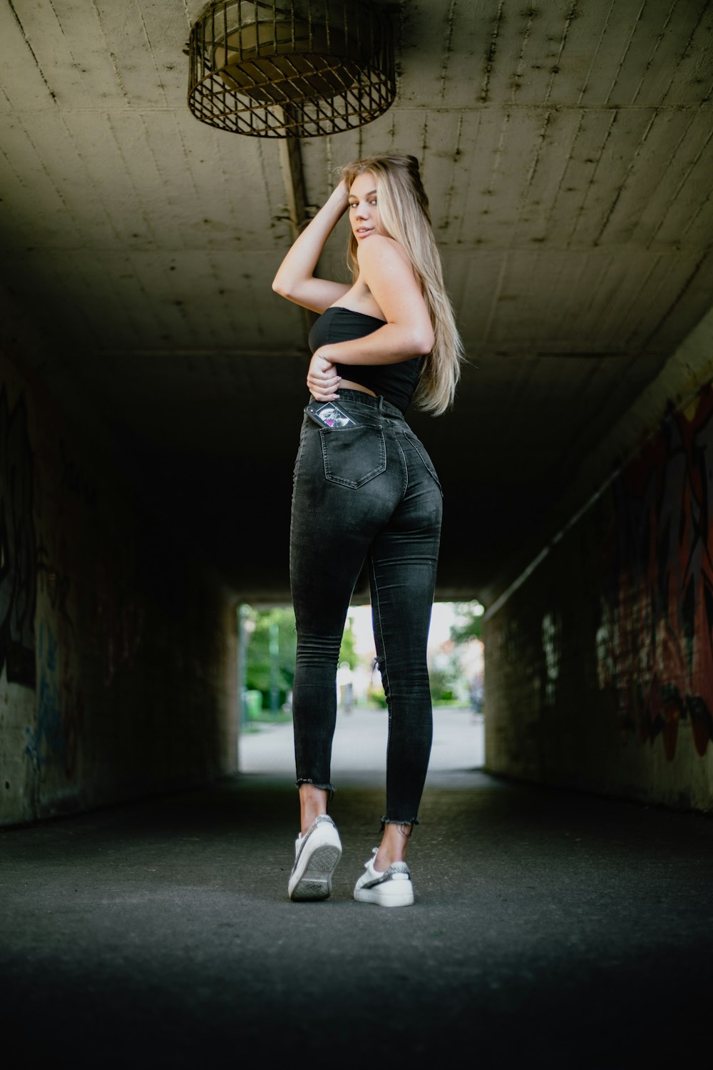 woman in black tank top and blue denim jeans standing on tunnel