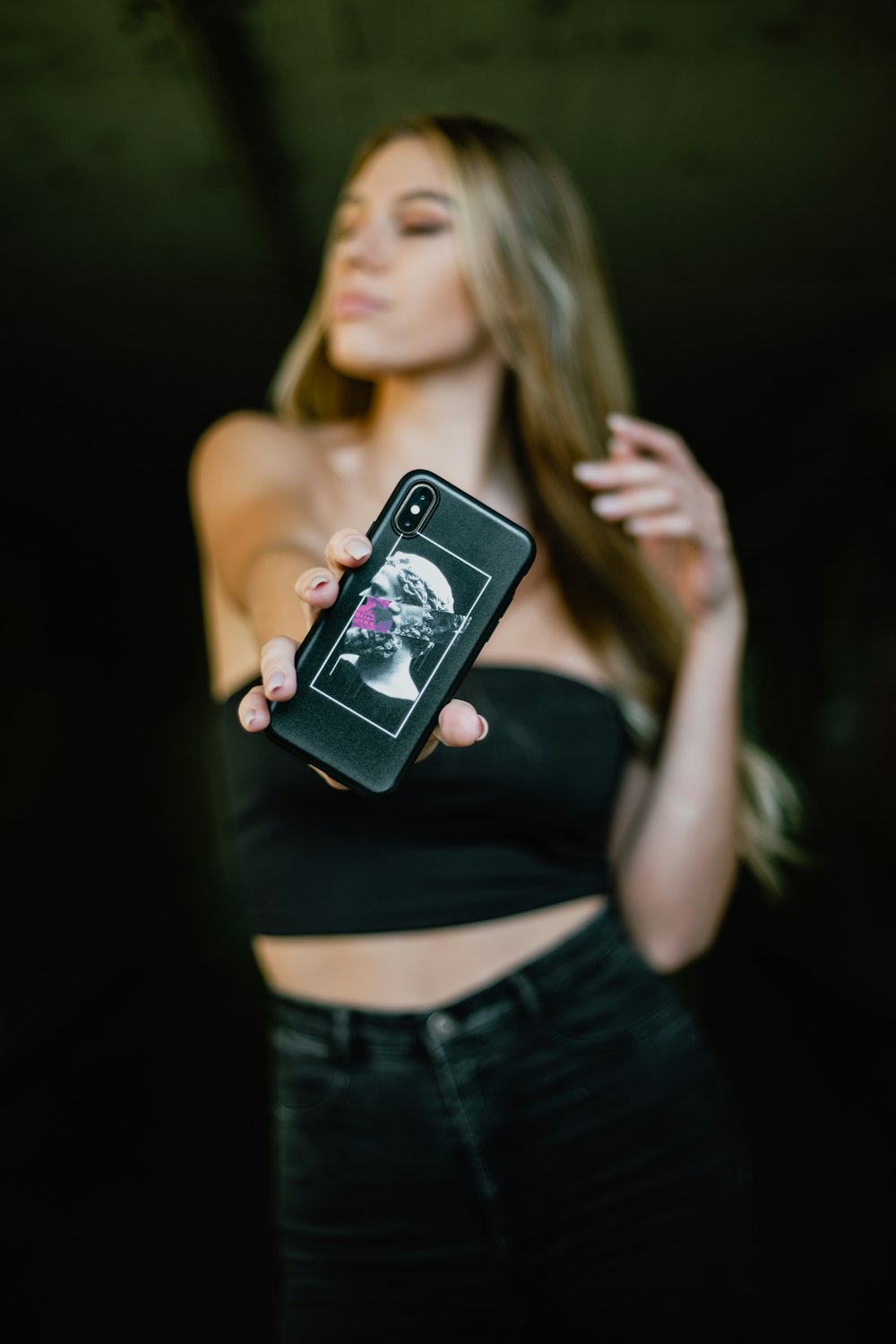 woman in black tank top and blue denim shorts holding black smartphone