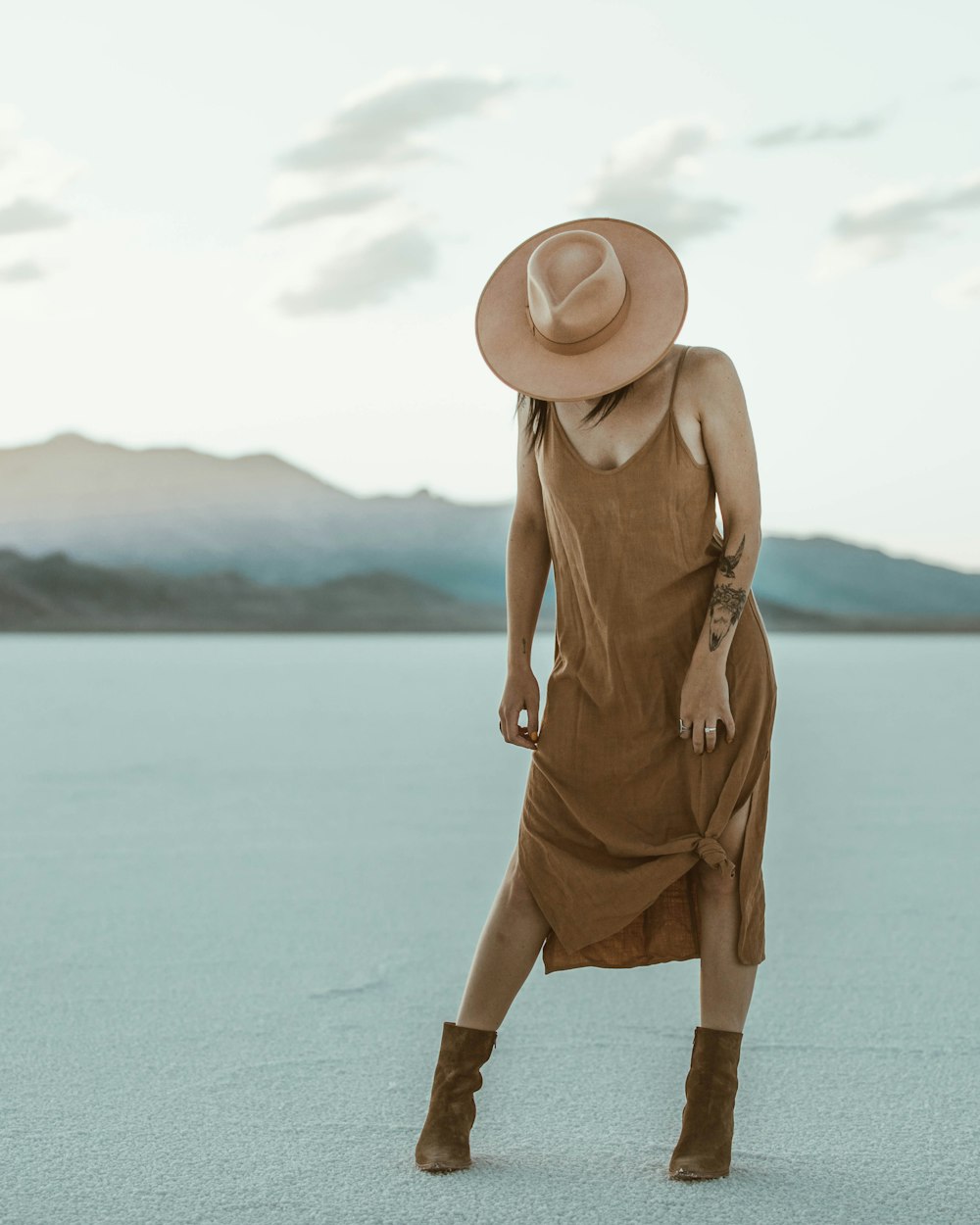 Frau in braunem Kleid mit braunem Sonnenhut, die tagsüber auf weißem Sand steht