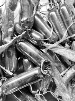 A collection of cylindrical objects wrapped tightly in plastic or some reflective material. They appear to be tied at the ends, creating a sealed package look. The image is in black and white.