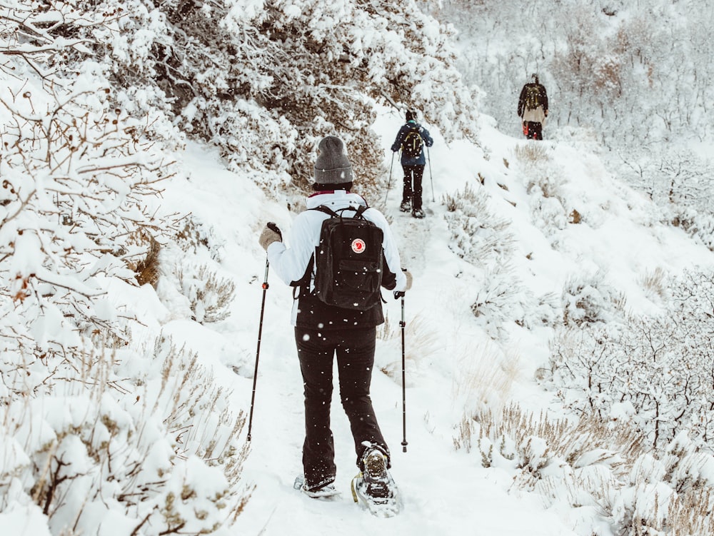 Persona con chaqueta negra y pantalones negros de pie en el suelo cubierto de nieve durante el día