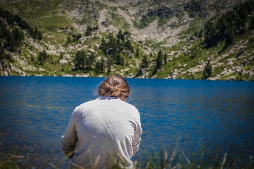 man in white long sleeve shirt sitting on green grass near body of water during daytime